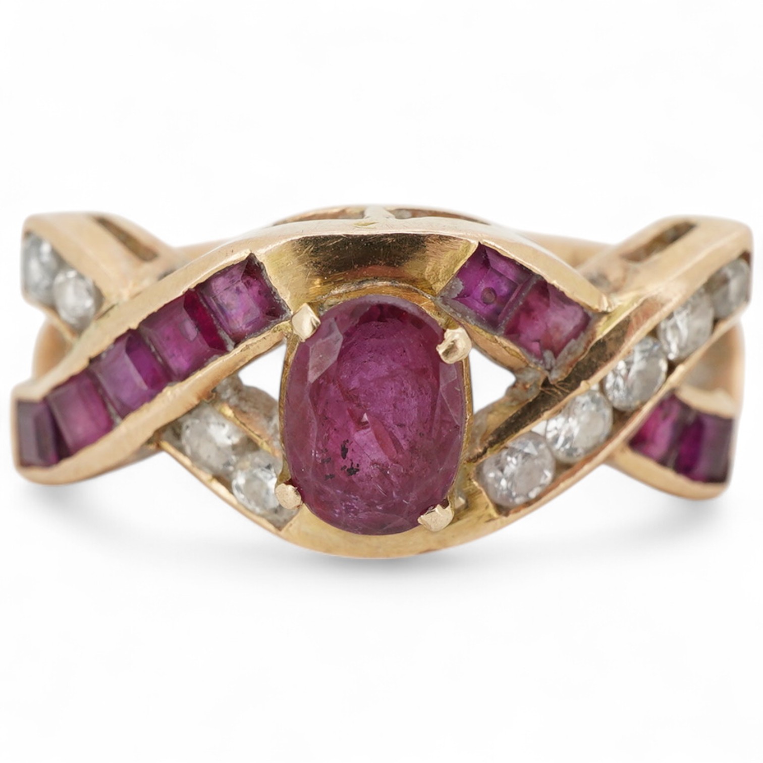 A ruby and diamond ring, of woven design, centring on an oval ruby, to a band set with calibré-cut rubies and brilliant-cut diamonds, mounted in gold, size N1/2, stamped 18K, gross weight 4 grams